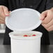 A person holding a white plastic lid over a container of tomatoes.