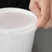 A person's hand opening a white Cambro plastic container with a lid.