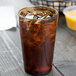 A Cambro amber plastic tumbler filled with brown liquid and ice on a table.