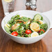 An Arcoroc serving bowl filled with salad with tomatoes, cucumbers, and other vegetables.