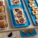 A blue Cambro market tray with a variety of pastries and muffins on a table.