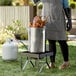 A woman using a Backyard Pro stainless steel turkey fryer to cook chicken on a grill.