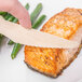 A person cutting a piece of salmon with an Eco-gecko heavy weight disposable wooden knife.