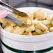 A person using tongs to serve croutons from a bowl on a counter.