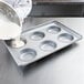 A chef pouring batter into a Chicago Metallic hamburger bun pan.