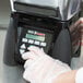 A person wearing plastic gloves using a Waring commercial blender on a counter in a professional kitchen.