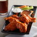 A plate of buffalo chicken wings coated in hot sauce, served with celery, carrot sticks, and dipping sauces.