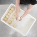 A person holding a ball of dough in a white tray.