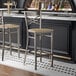 A metal bar stool with a cross back design and a driftwood-finished wooden seat.