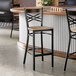 A black metal bar stool with a cross back design and a driftwood-colored wooden seat.
