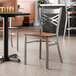 A metal cross back chair with a clear coat finish and an antique walnut wood seat.