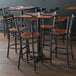 A Lancaster Table & Seating black finish cross back bar stool with a wooden seat on a table in a restaurant.