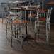 A Lancaster Table & Seating clear coat finish cross back bar stool with an antique walnut wood seat on a table in a restaurant dining area.