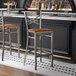 A metal bar stool with a cross back design and an antique walnut wood seat.
