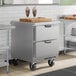 A compact stainless steel worktop refrigerator with two drawers and caster wheels.
