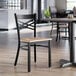 A black metal cross back chair with a light wood driftwood seat, designed for dining or restaurant use.