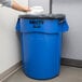 A person's arm in a white shirt wiping a blue Rubbermaid trash can with a paper towel.