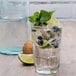 A glass of water with ice, limes, and blueberries on a white background.