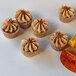 A group of white cupcakes with frosting and fruit slices on a table.