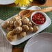 An American Metalcraft rectangular melamine serving platter with a plate of food and a bowl of red sauce on a table.