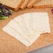 A cutting board with slices of Cooper Black Pepper Sharp White American Cheese, bread, and salad.