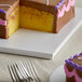 A slice of chocolate frosted cake with purple icing on a white Enjay square cake drum.