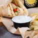 A sandwich and chips on a table with a bowl of white Kronos Tzatziki sauce.