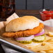 A table with a tray holding a chicken sandwich with pickles and onions, a glass of ketchup, and fries.