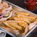 A tray of a sandwich, Saint-Arneault Golden Crop fries, and a pickle with a glass of ketchup on the side.