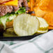 A plate of food with a burger and potato chips, a slice of Patriot Pickle next to it.