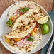 A plate with two tacos made with Father Sam's flour tortillas, chicken, and vegetables with a lime wedge.