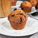 A Bake'n Joy chocolate chip muffin on a plate with a cup of coffee.