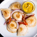 A plate of CHEEMO Three Cheese Pierogies with yellow sauce.