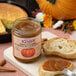 A jar of Kime's pumpkin butter spread on a cutting board next to a slice of bread.