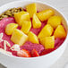 A bowl of fruit smoothie with mango, pineapple, and strawberries.