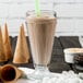 A glass of J. Hungerford Smith chocolate milkshake with a straw, marshmallows, and chocolates on the table.