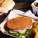 A hand holding a breaded veal patty sandwich with vegetables.