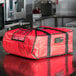 A red Rubbermaid ProServe insulated pizza delivery bag on a counter.