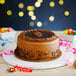 A chocolate cake on a white Enjay round cake drum on a table in a bakery display.