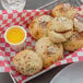 A basket of food with a Grandioso garlic sauce dipping cup on a checkered tablecloth.