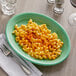 A Tuxton Cilantro oval china platter with a plate of macaroni and cheese and a fork.