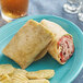 A blue plate with a Father Sam's Bakery Sundried Tomato tortilla, a burrito, and chips on a table.