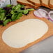 Sliced BelGioioso Mild Provolone Cheese on a cutting board with bread and vegetables.