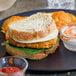 A plate with a sandwich with BelGioioso Mild Provolone cheese, spinach, and vegetables and potato wedges.