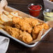 A tray of Tyson Red Label chicken tenderloin fritters and french fries with a glass cup of ketchup.