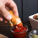 A person dipping a Tyson Red Label chicken tender into a small glass of ketchup.