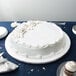 A white Enjay round cake drum under a white frosted cake on a table.