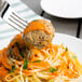 A fork with Casa Di Bertacchi Italian style beef meatballs and spaghetti with sauce on a plate.