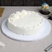 A plain white round cake with minimal floral decorations on top, displayed on a thick white cake drum.