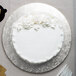 A white cake with frosting and flowers on a silver Enjay round cake drum.